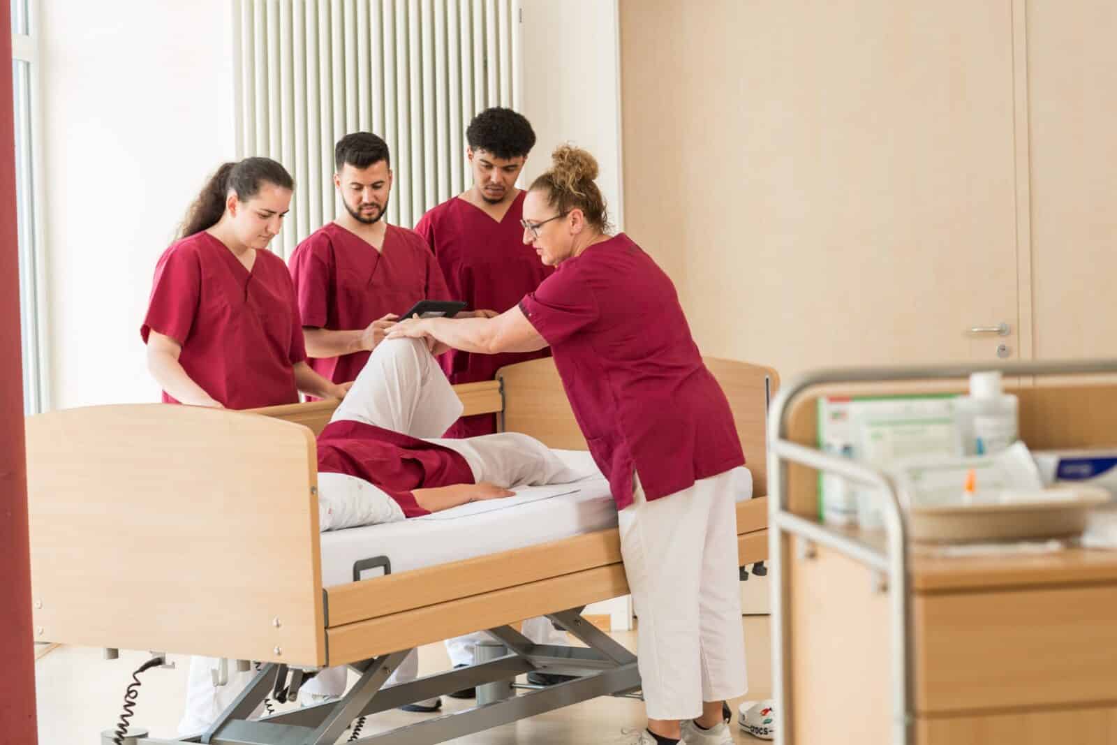 Auszubildende und eine Lehrkraft üben am Pflegebett die Lagerung einer Person