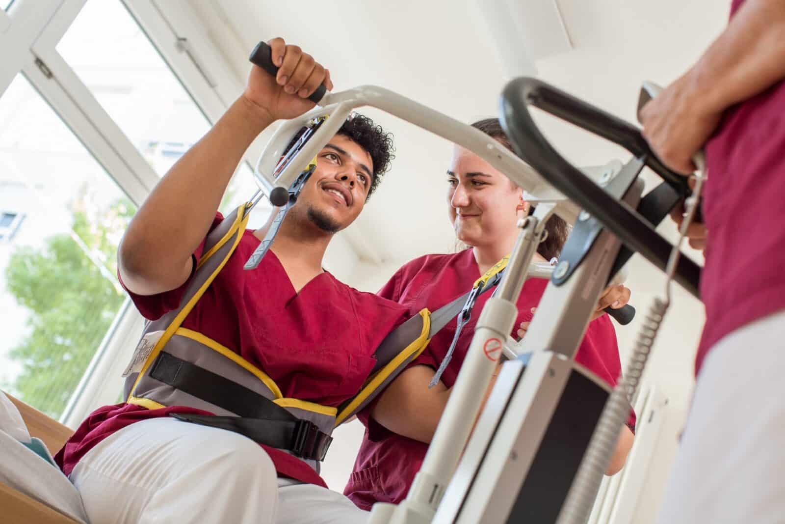 Ein Auszubildender übt mit einem Patientenlifter, eine Kollegin schaut zu