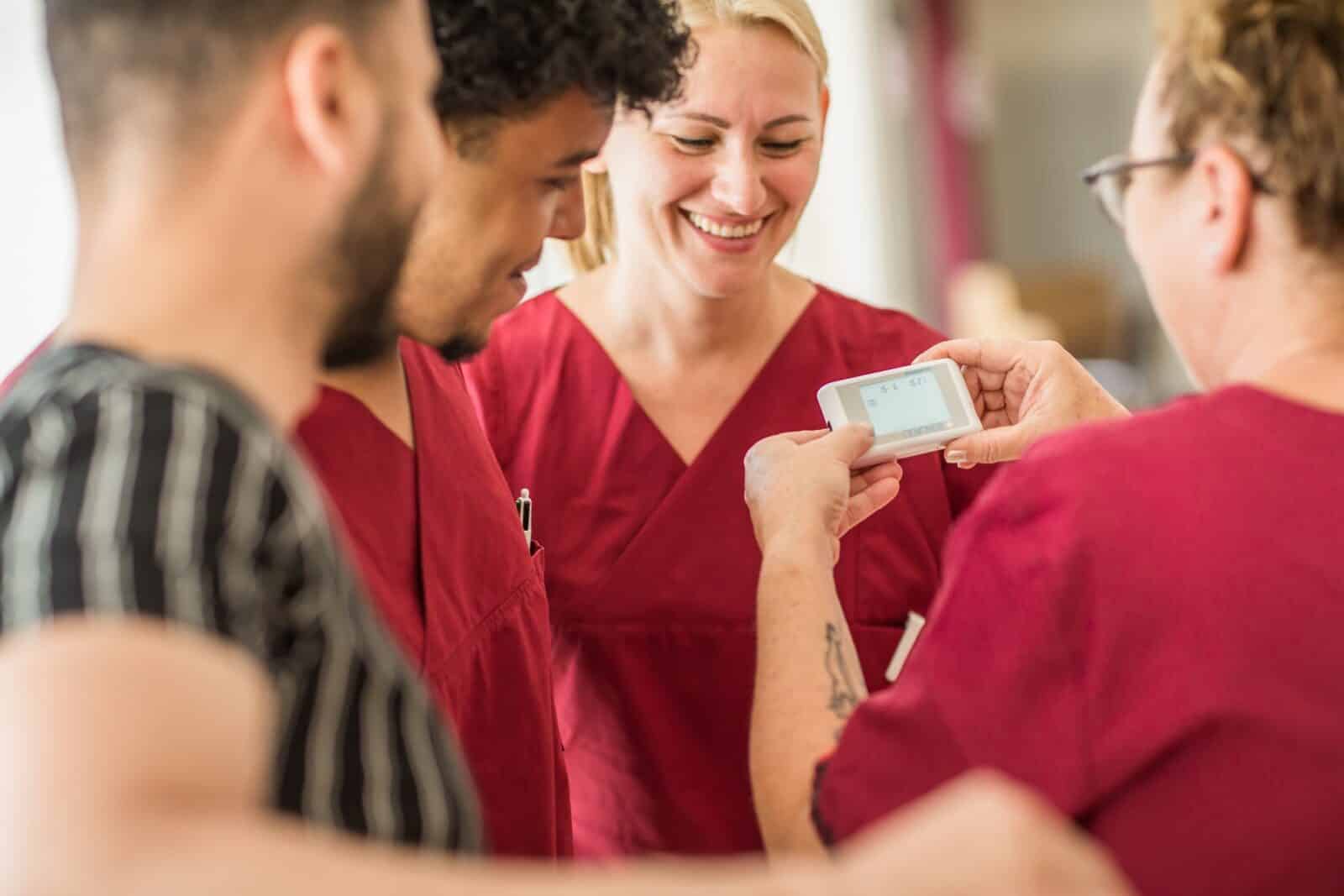 Auszubildende in roter Pflegekleidung betrachten ein medizinisches Messgerät