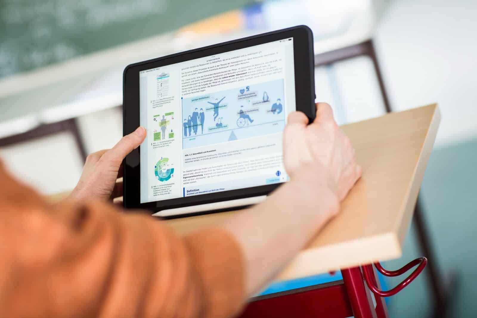 Hände halten ein Tablet mit digitalem Lehrmaterial